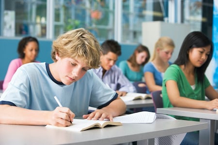 Student reading a book at his desk in a classroom