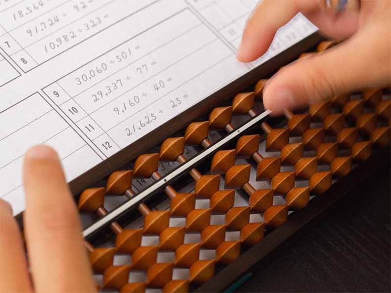 Child practicing long division problems on a worksheet with an abacus