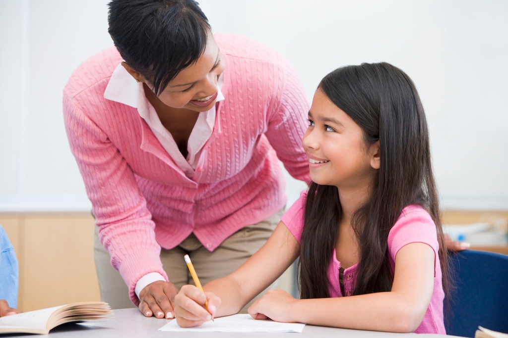Teacher helping an elementary student write words correctly
