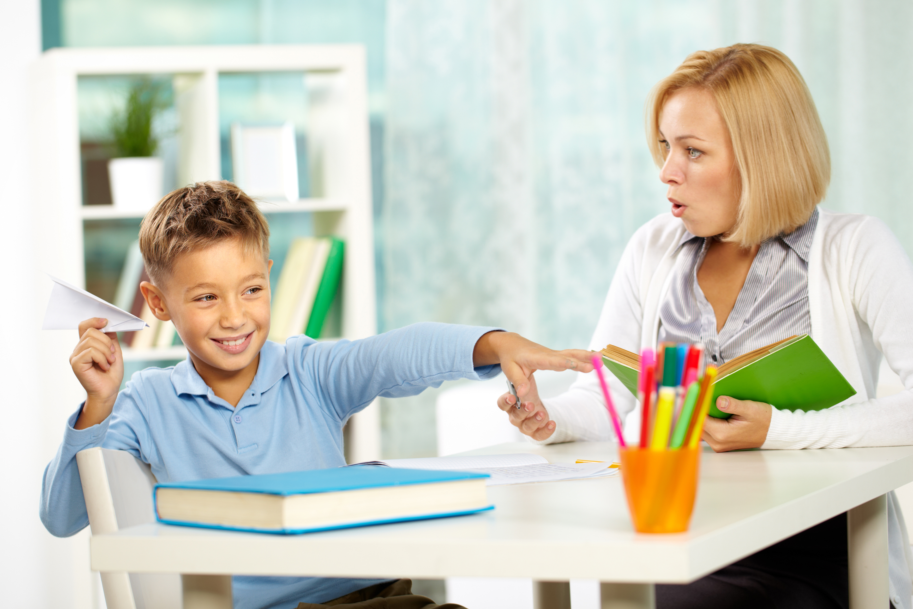 portrait-of-naughty-boy-playing-with-paper-plane-at-workplace-and-his-indignant-tutor-looking-at-him