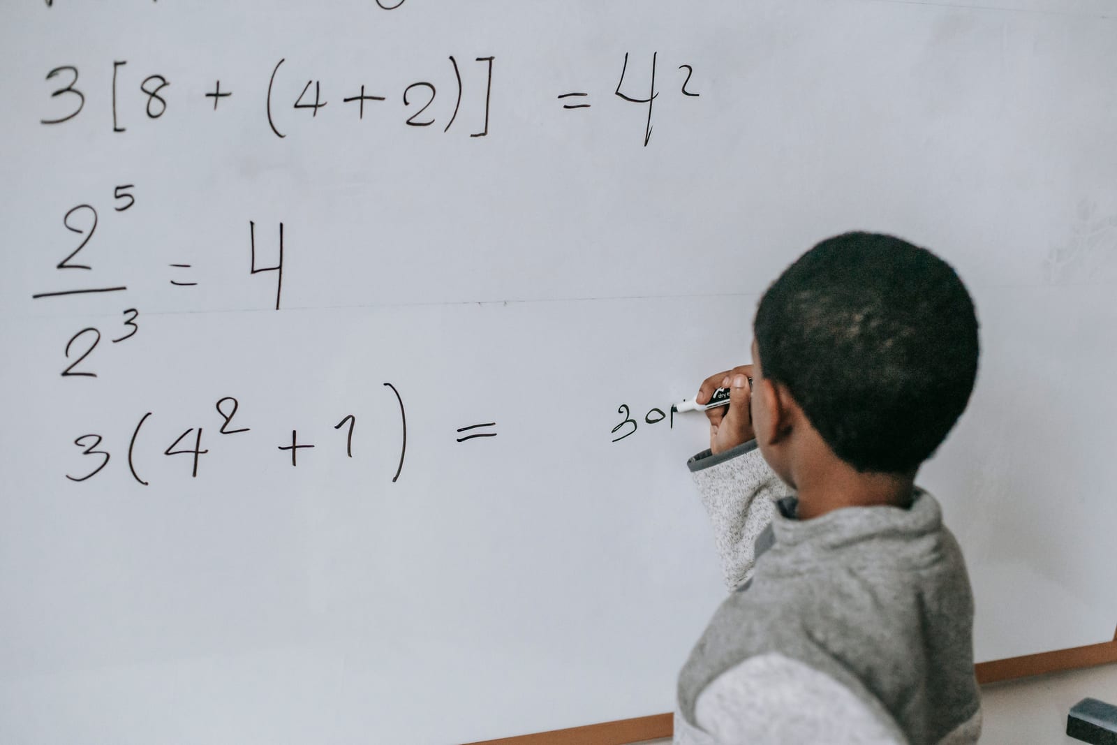 A young student solving order-of-operations problems on a whiteboard