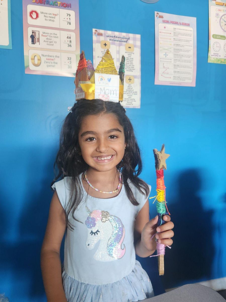 A Genie Academy camper wearing a handmade paper crown and holding a rainbow-wrapped wand she built at camp