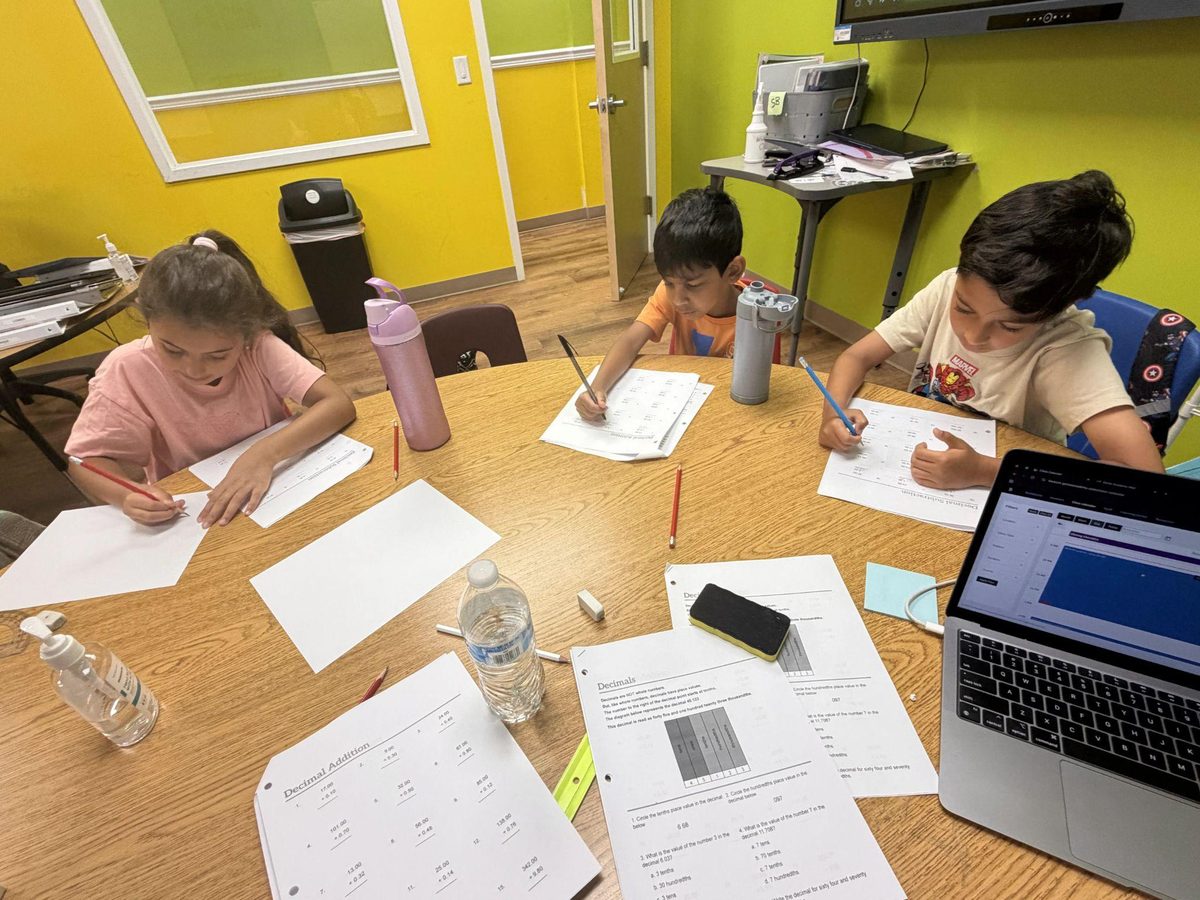 Three Genie Academy campers working through decimal addition and subtraction worksheets at a table