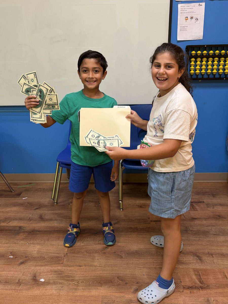 Two Genie Academy campers holding play money and a folder during a summer camp money-math activity