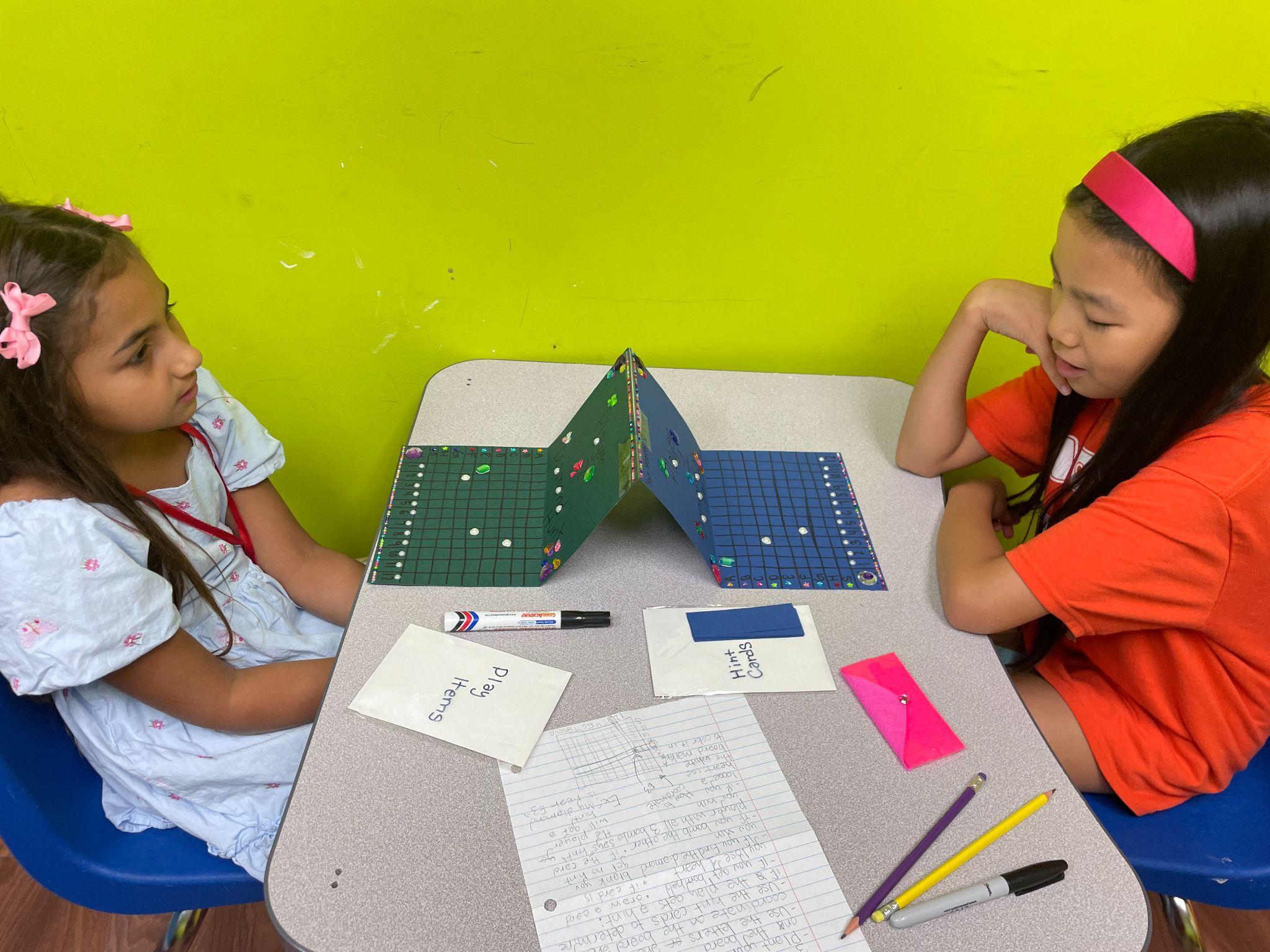 Two campers playing a handmade coordinate-grid board game they built themselves