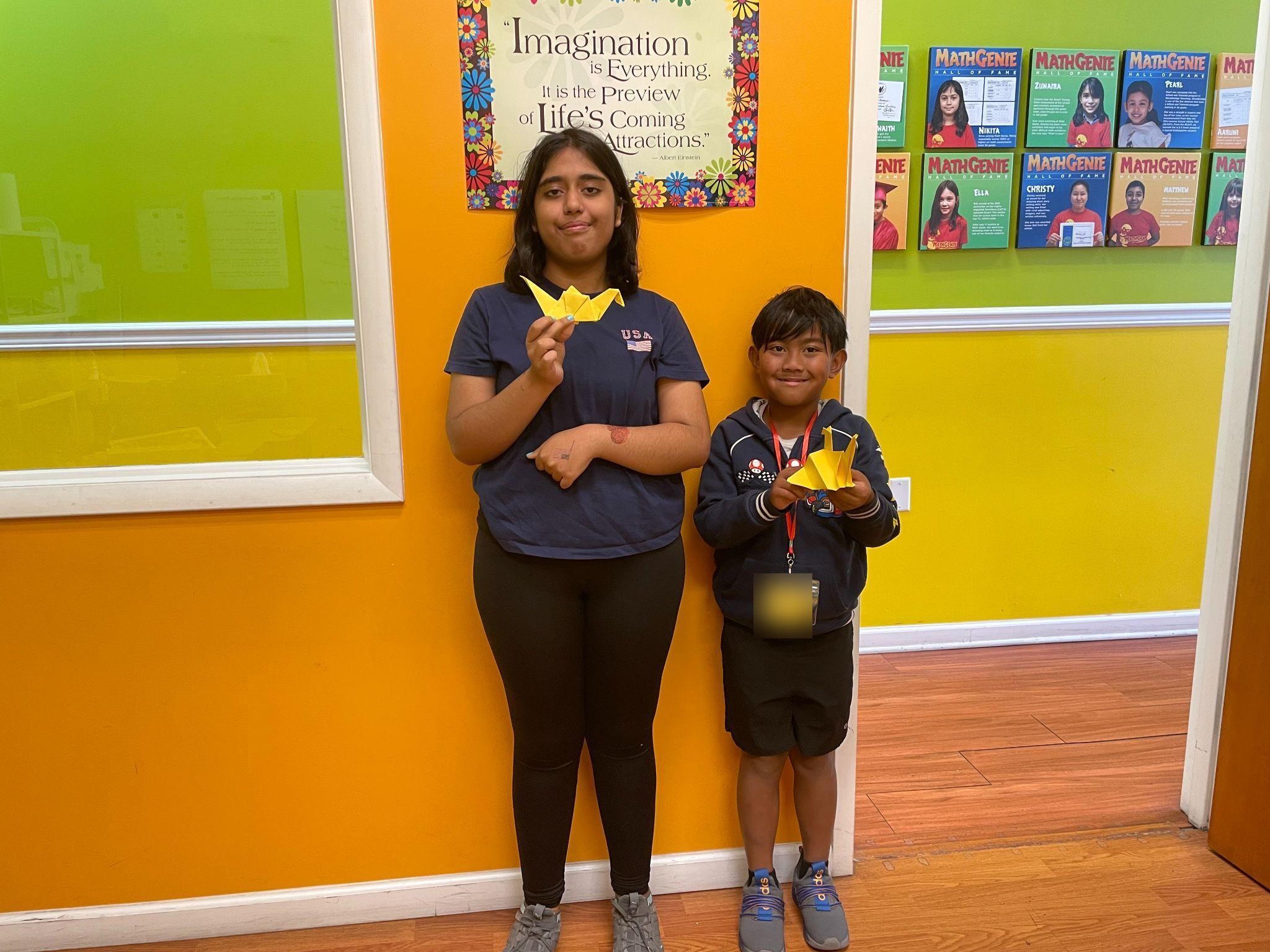 Two campers proudly holding up the yellow origami cranes they folded