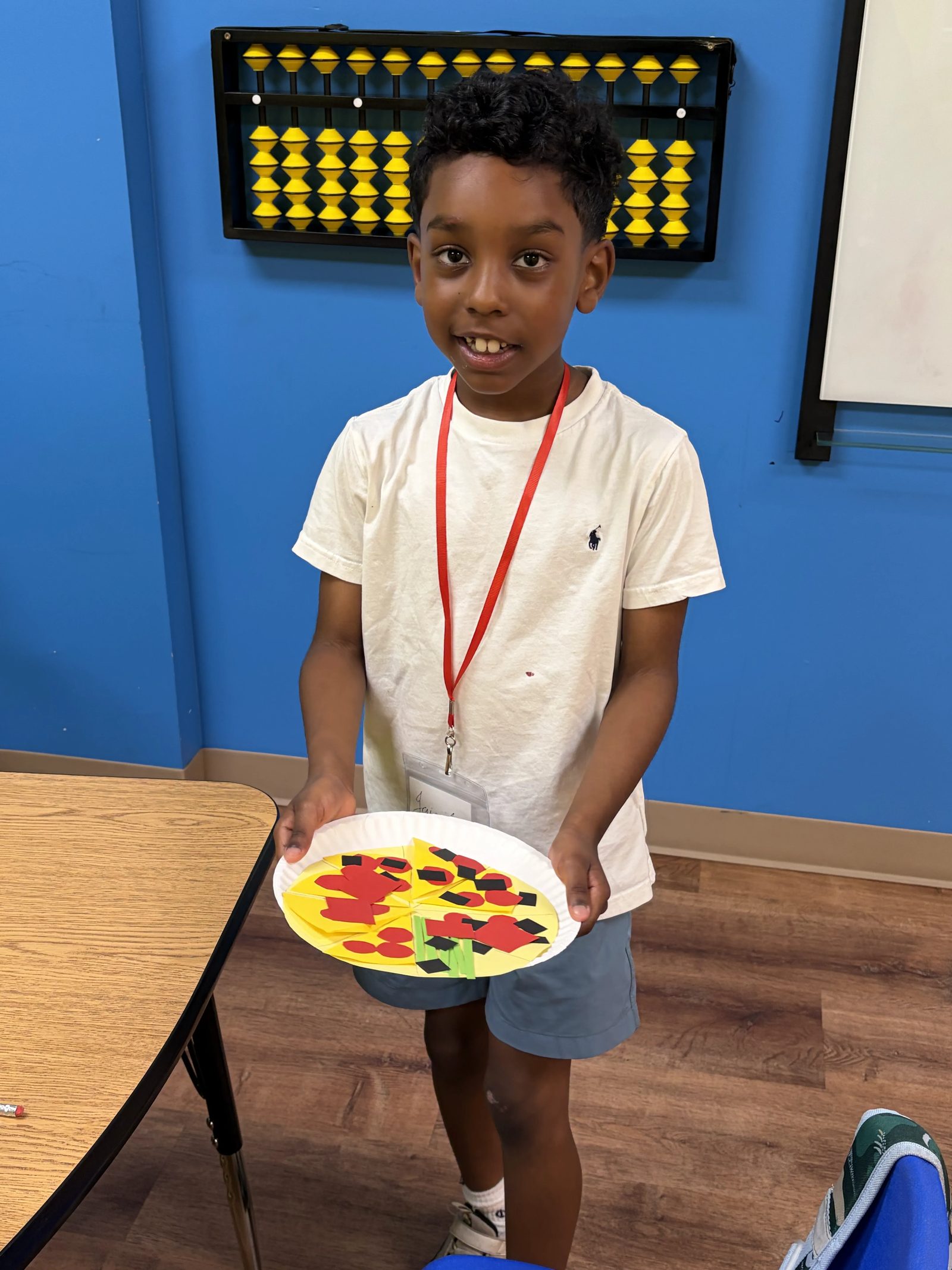 A camper smiles while holding up a paper-plate craft designed to look like a pizza