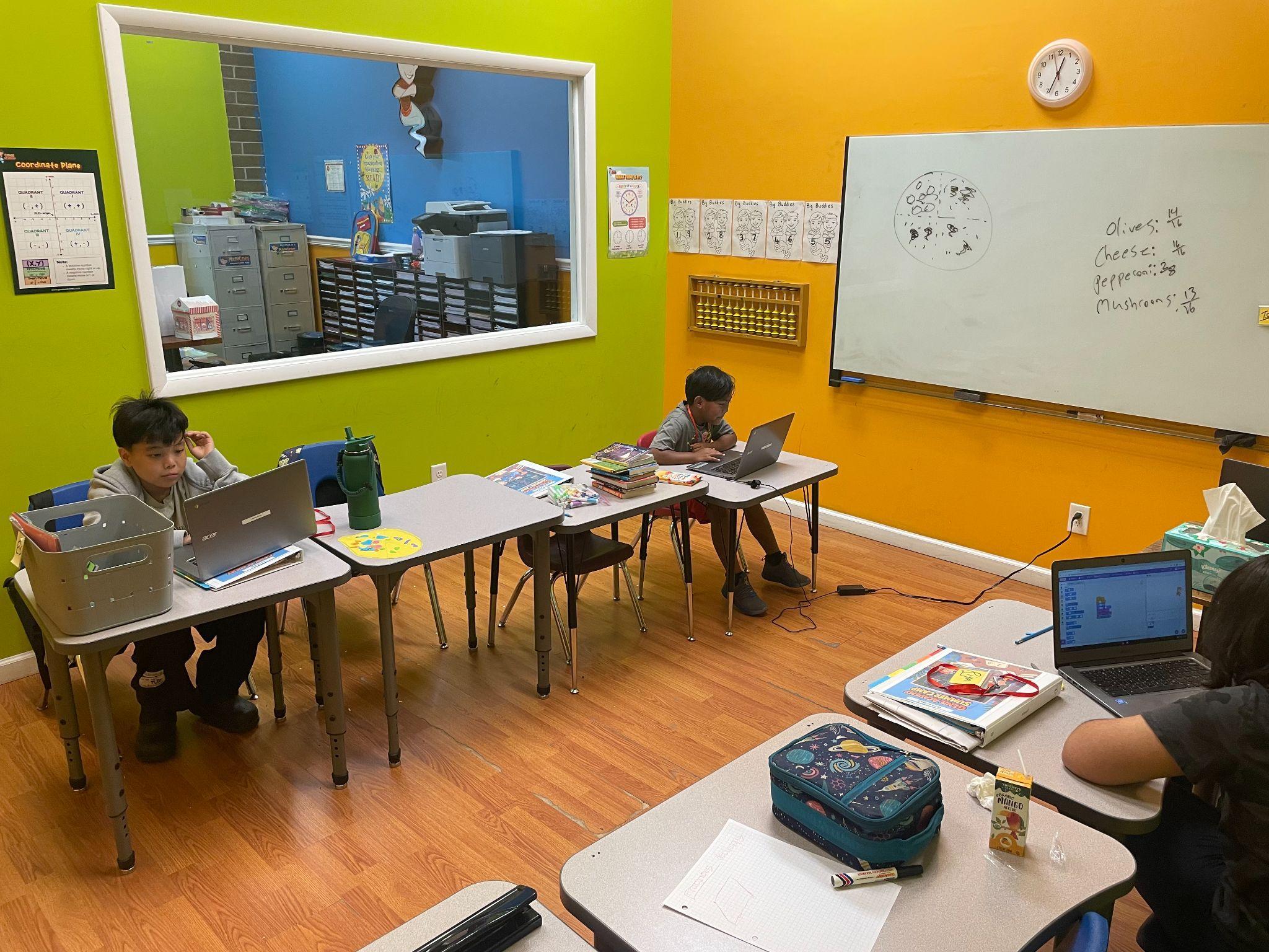A camp classroom where fractions are taught with a pizza drawing on the whiteboard while campers work on laptops