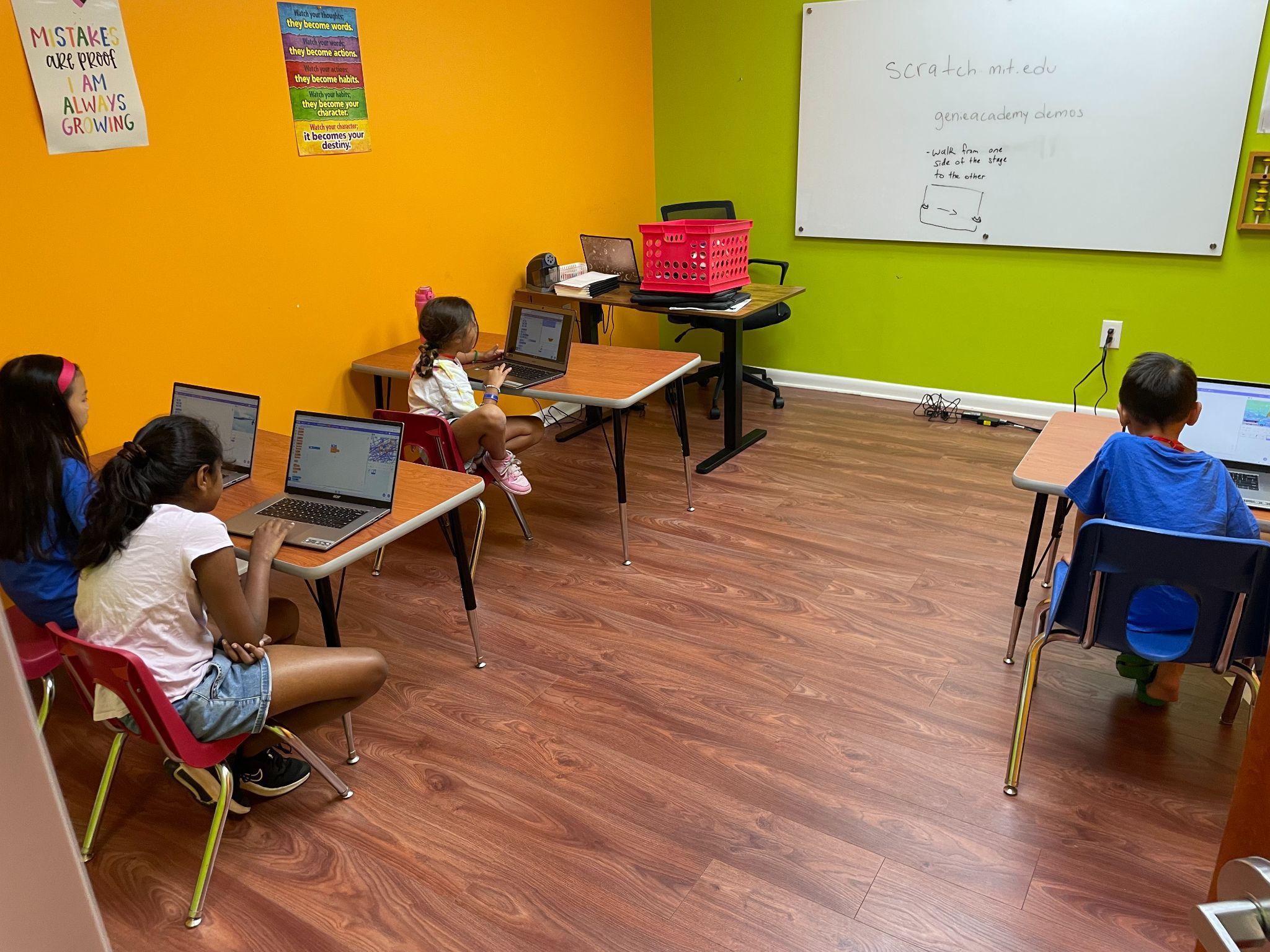 Campers building Scratch coding projects on laptops in a Genie Academy camp room